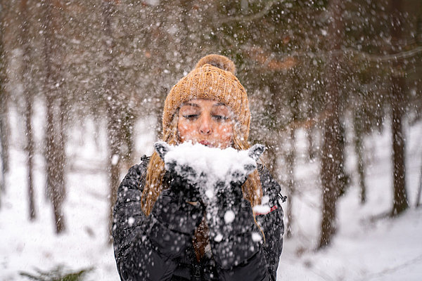 Ein Mädchen, dass im Schnee steht und in die Kamera den Schnee in ihrer Hand pustet. 
